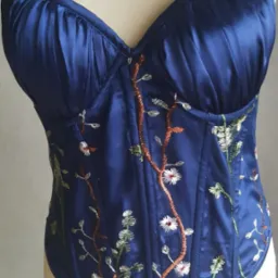 Niebieski satynowy gorset z haftowanymi motywami roślinnymi, eksponowany na manekinie.