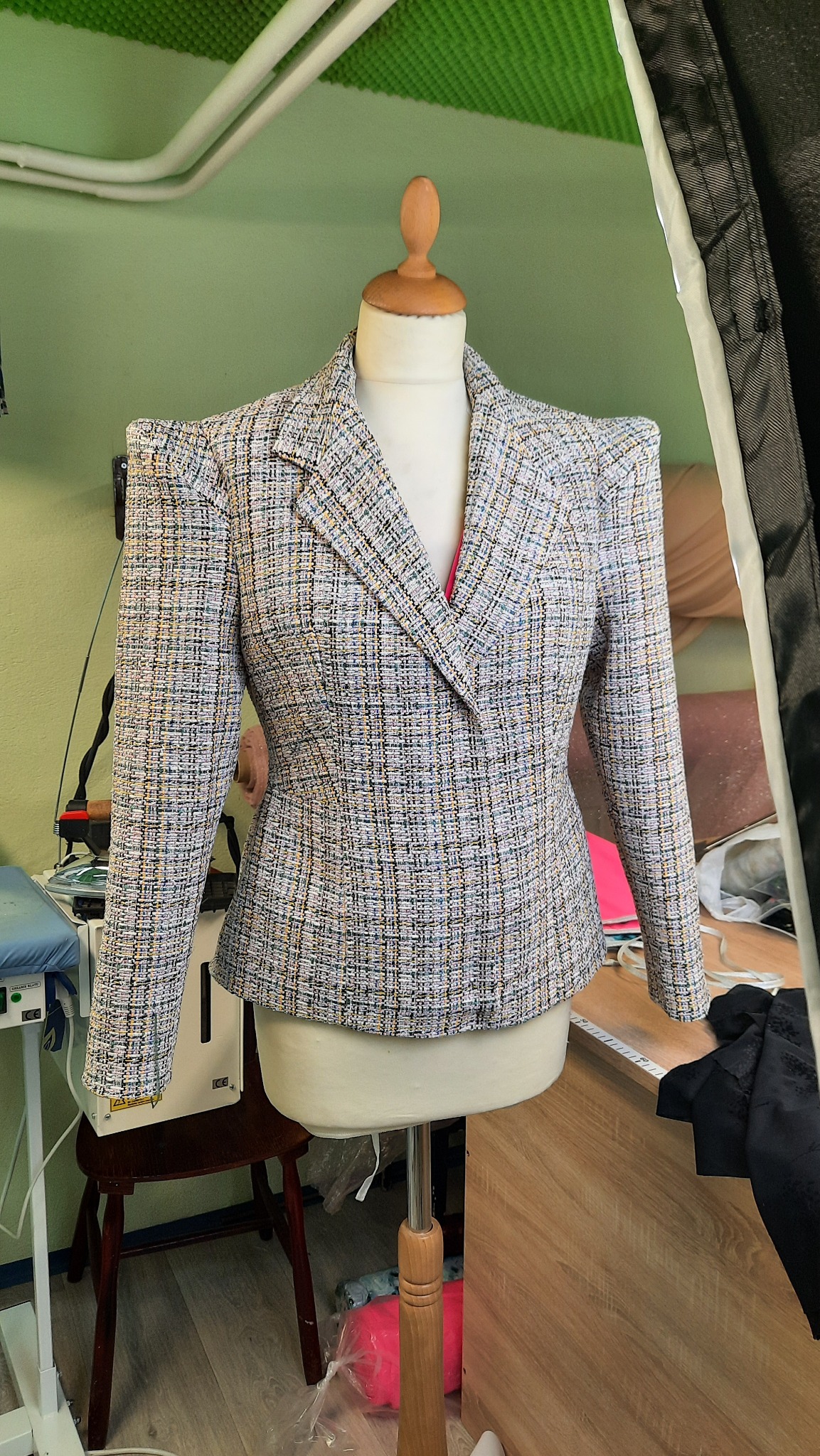 Damski żakiet w drobną kratę, z wyraźnie zaznaczoną talią i ramionami, prezentowany na manekinie krawieckim w pracowni.