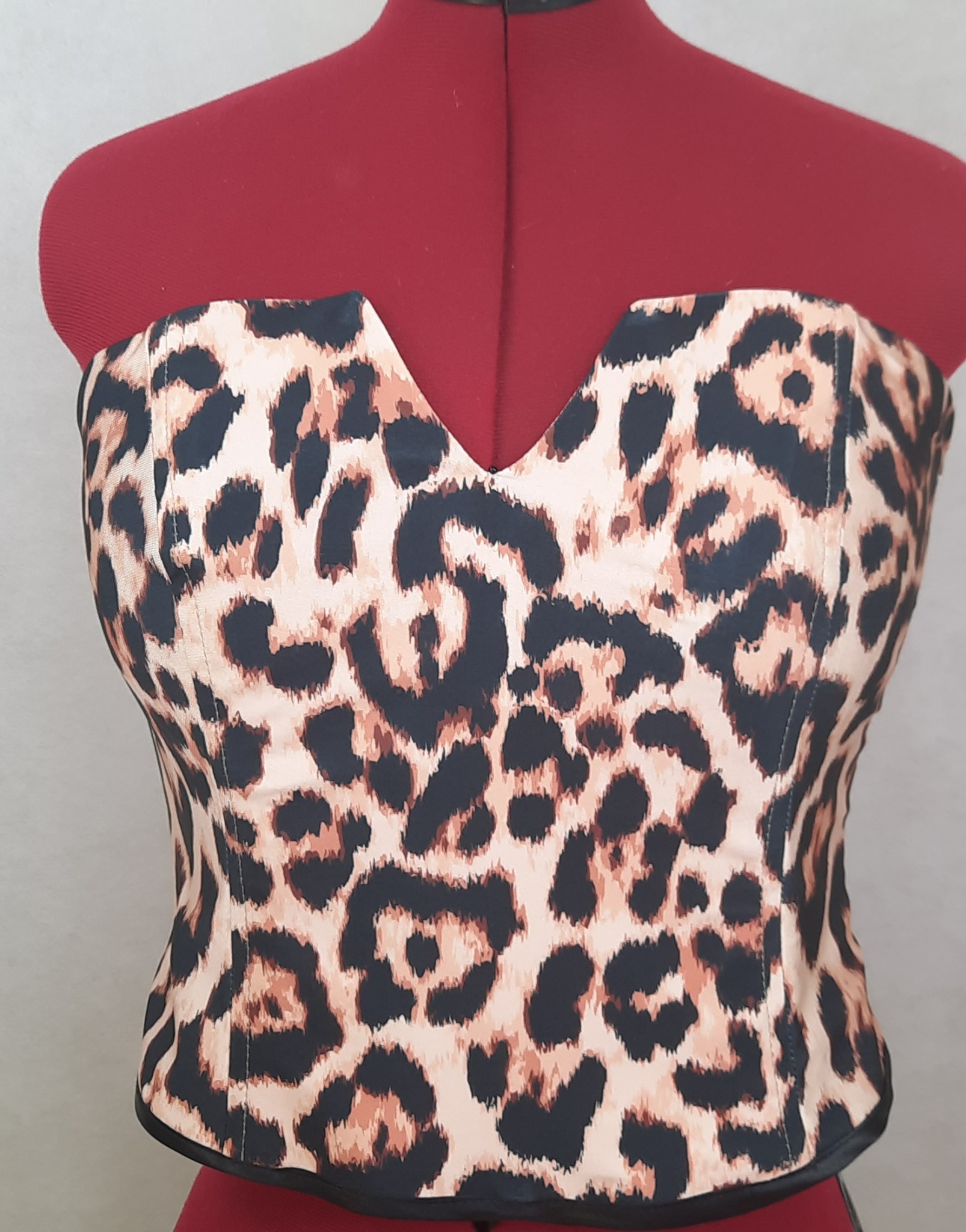 Gorset z materiału w panterkę, z dekoltem w szpic, umieszczony na czerwonym manekinie krawieckim.