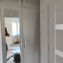 Wojtek Wojnarowski - Szara szafa z lustrzanymi drzwiami, w odbiciu widoczny odkurzacz przemysłowy i narzędzia, sugerujące prace montażowe w trakcie realizacji.