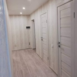 Dream_house_pl_ua - Korytarz po odświeżeniu: ściany pokryte tapetą w odcieniach beżu i szarości, jasna podłoga imitująca drewno, dwie białe, panelowe drzwi z srebrnymi klamkami, oświetlenie sufitowe punktowe.