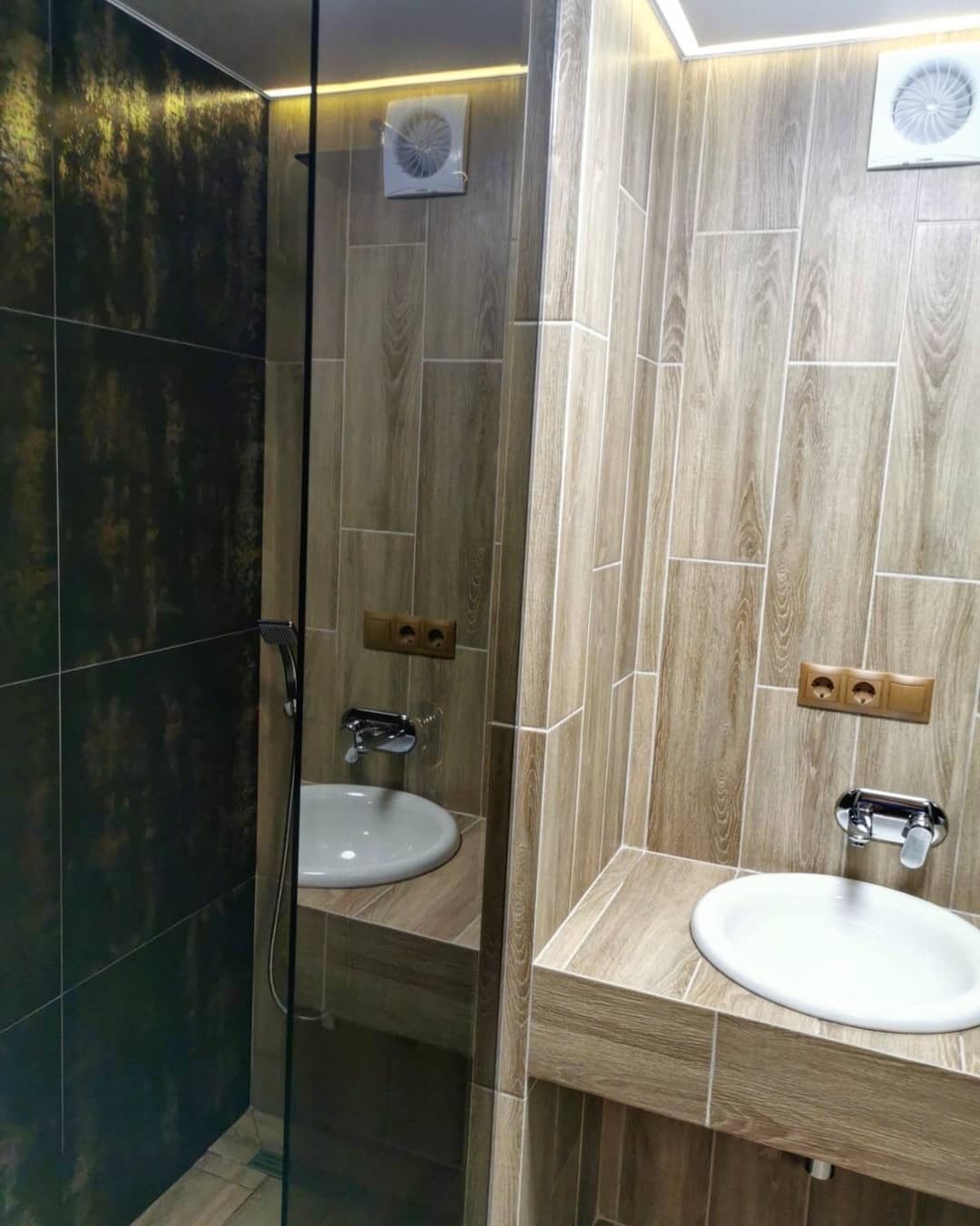 Nowoczesna łazienka z kabiną prysznicową oddzieloną szybą, wykończona płytkami imitującymi drewno, z umywalką nablatową i wentylatorem sufitowym.