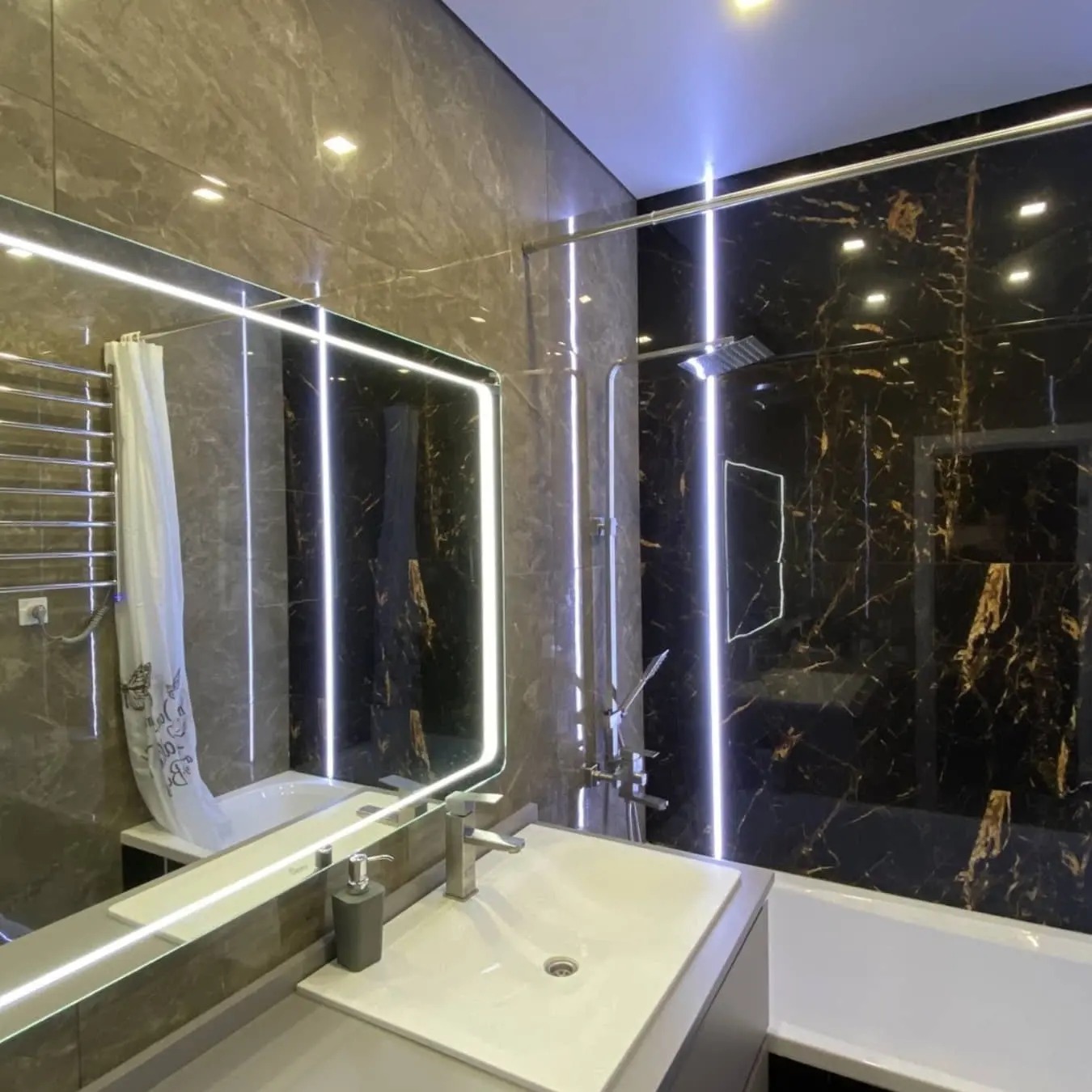 Nowoczesna łazienka z brązowo-czarnymi marmurkowymi płytkami, podświetlanym lustrem i minimalistyczną armaturą, akcentująca elegancki design i funkcjonalne oświetlenie.