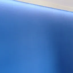 Niebieska ściana z delikatną teksturą w jodełkę, oświetlona od góry listwą LED, widoczny fragment białej ściany i drzwi.