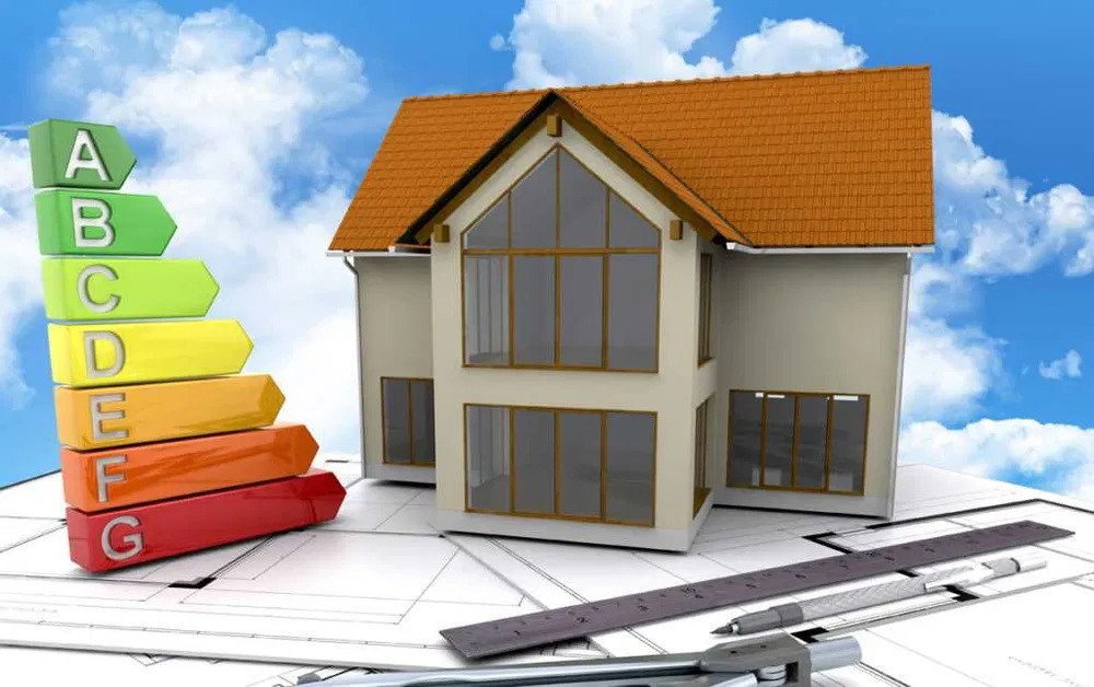 Dwukondygnacyjny dom z brązowym dachem, obok niego skala efektywności energetycznej A-G, leżący na planach architektonicznych z narzędziami kreślarskimi, na tle błękitnego nieba z chmurami.