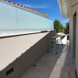 Marcin Gregorczyk - Zewnętrzna ściana budynku z zamontowaną szklaną balustradą, widoczny fragment elewacji i drabina aluminiowa.