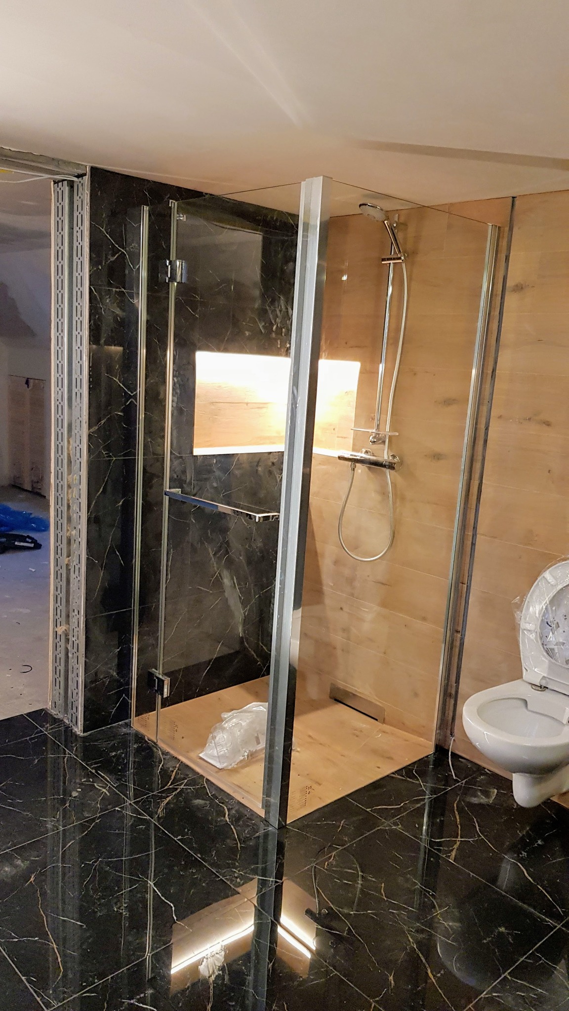 Montaż kabiny prysznicowej z czarnymi marmurowymi płytkami na ścianach i podłodze, widoczna toaleta z otwartą klapą i folia zabezpieczająca na dnie kabiny.