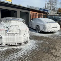 Dwa samochody marki Mercedes pokryte pianą podczas mycia na zewnątrz myjni, widoczne tablice rejestracyjne i logo Suzuki Serwis w tle.