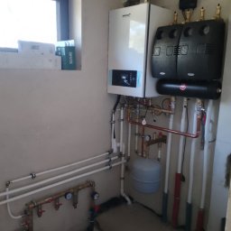 ZALST STEFAN STADNIK - Nowoczesny piec gazowy kondensacyjny z osprzętem zamontowany w kotłowni. Widoczne rury instalacji centralnego ogrzewania i elementy armatury.