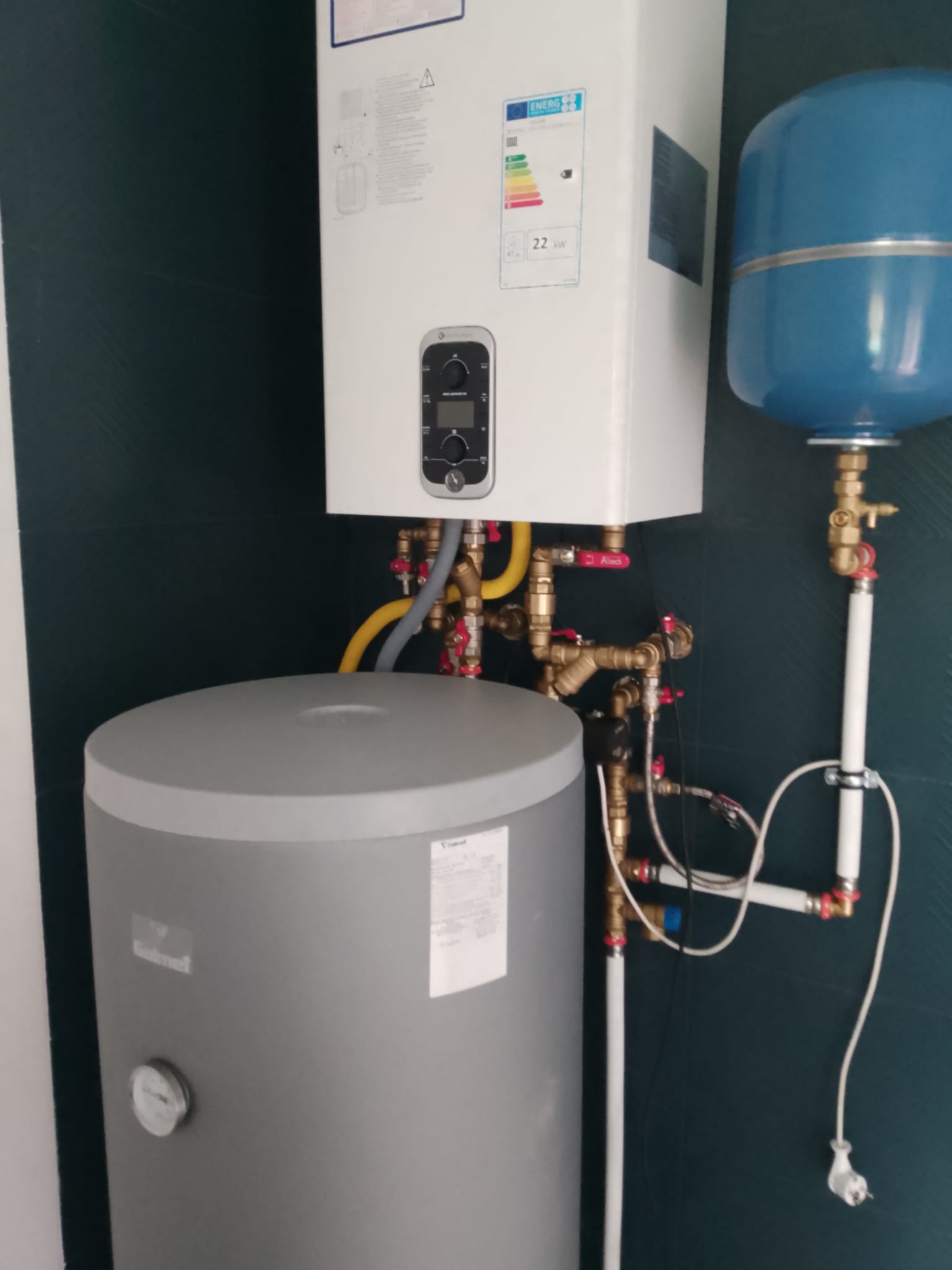 Zestaw kotła gazowego z zasobnikiem i naczyniem wzbiorczym. Widoczne liczne rury i zawory. Nowoczesny montaż instalacji grzewczej w kotłowni.