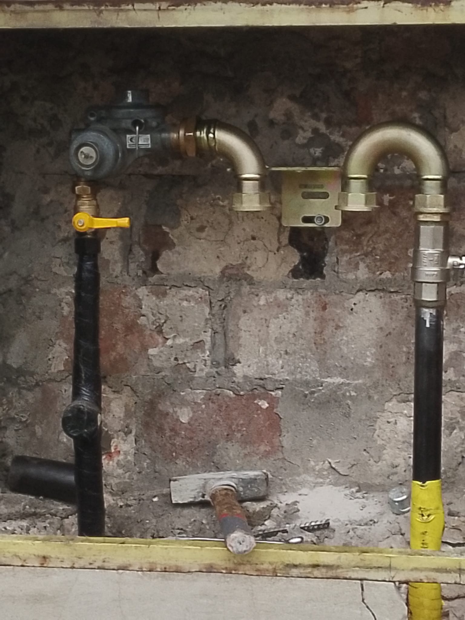 Szczegółowe ujęcie nowej instalacji gazowej z zaworem i rurami miedzianymi, zamontowanej na tle surowej ściany z cegły. Widoczne narzędzia.