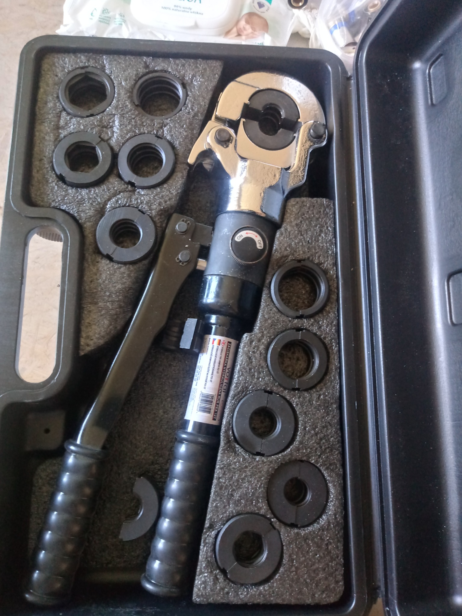 Zaciskarka hydrauliczna do rur PEX z zestawem matryc w czarnym futerale z wytłoczką z pianki, widoczne oznaczenia producenta na urządzeniu.