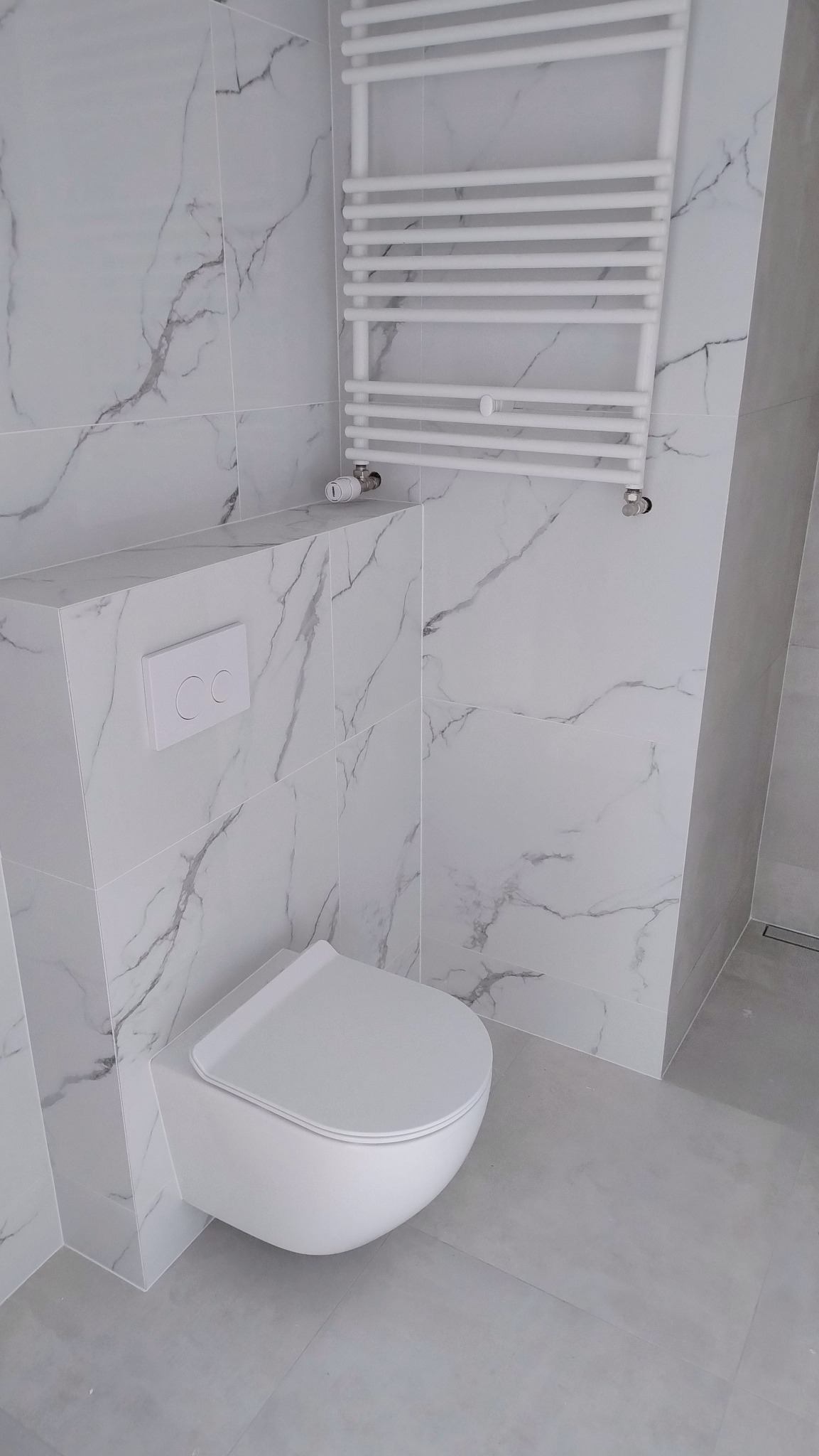 Nowoczesna toaleta podwieszana z marmurową okładziną ścienną i grzejnikiem drabinkowym w wykończonej łazience.