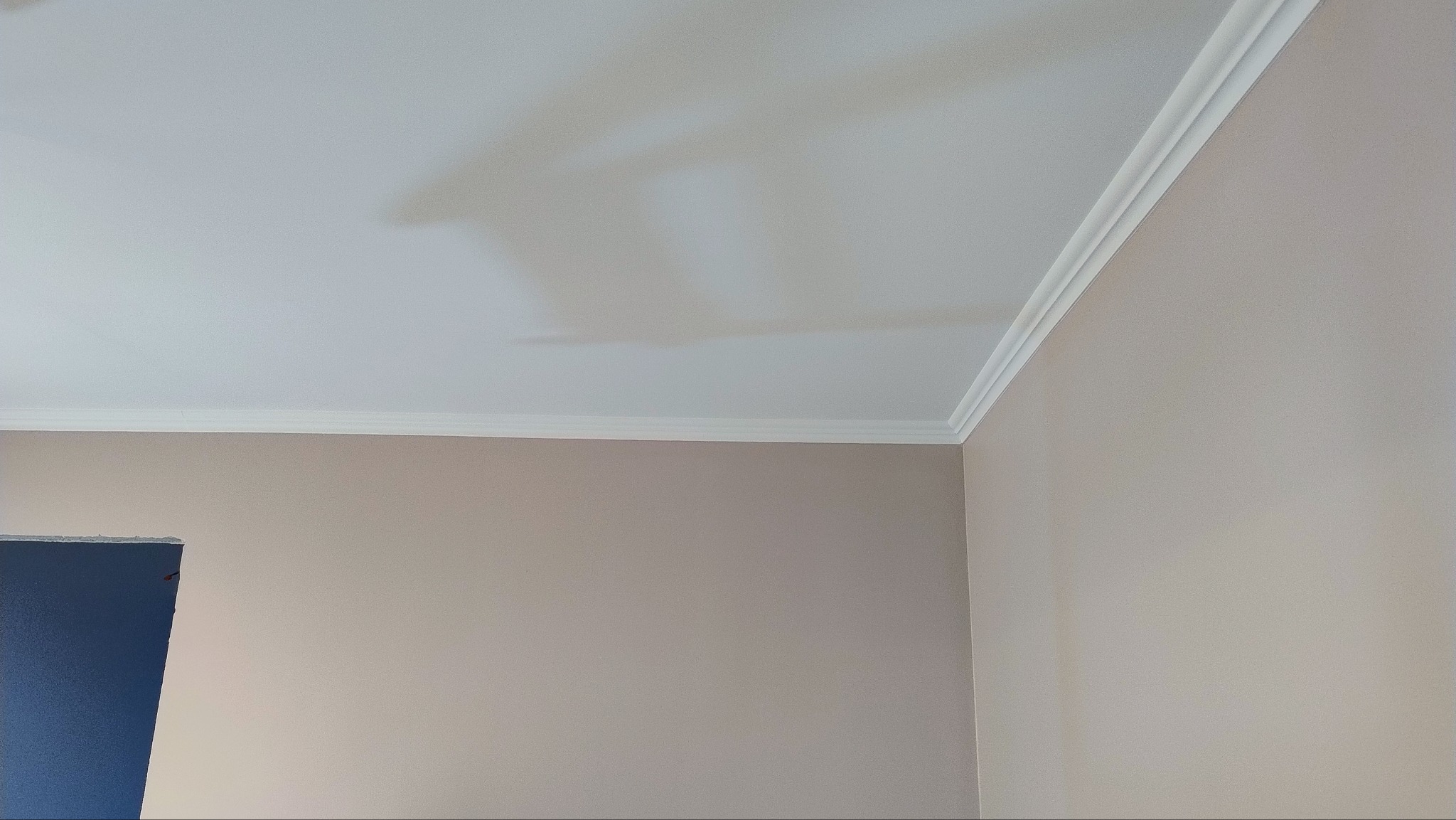 Pomieszczenie po remoncie: ściany pomalowane na beżowo, biały sufit z dekoracyjną listwą przysufitową, widoczny fragment niebieskiego zabezpieczenia.