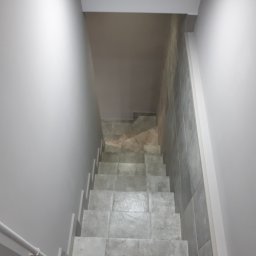 FAST BILDING VASYL VOLOSHYN - Schody wyłożone szarymi płytkami, widok z góry, ściany pomalowane na szaro, minimalistyczny design.