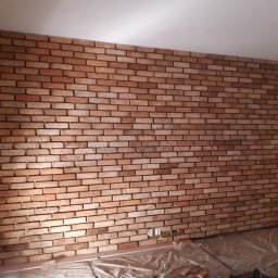 FAST BILDING VASYL VOLOSHYN - Ściana wykończona czerwoną cegłą klinkierową, widoczne gniazdka elektryczne, podłoga zabezpieczona folią malarską, pozostałości zaprawy.