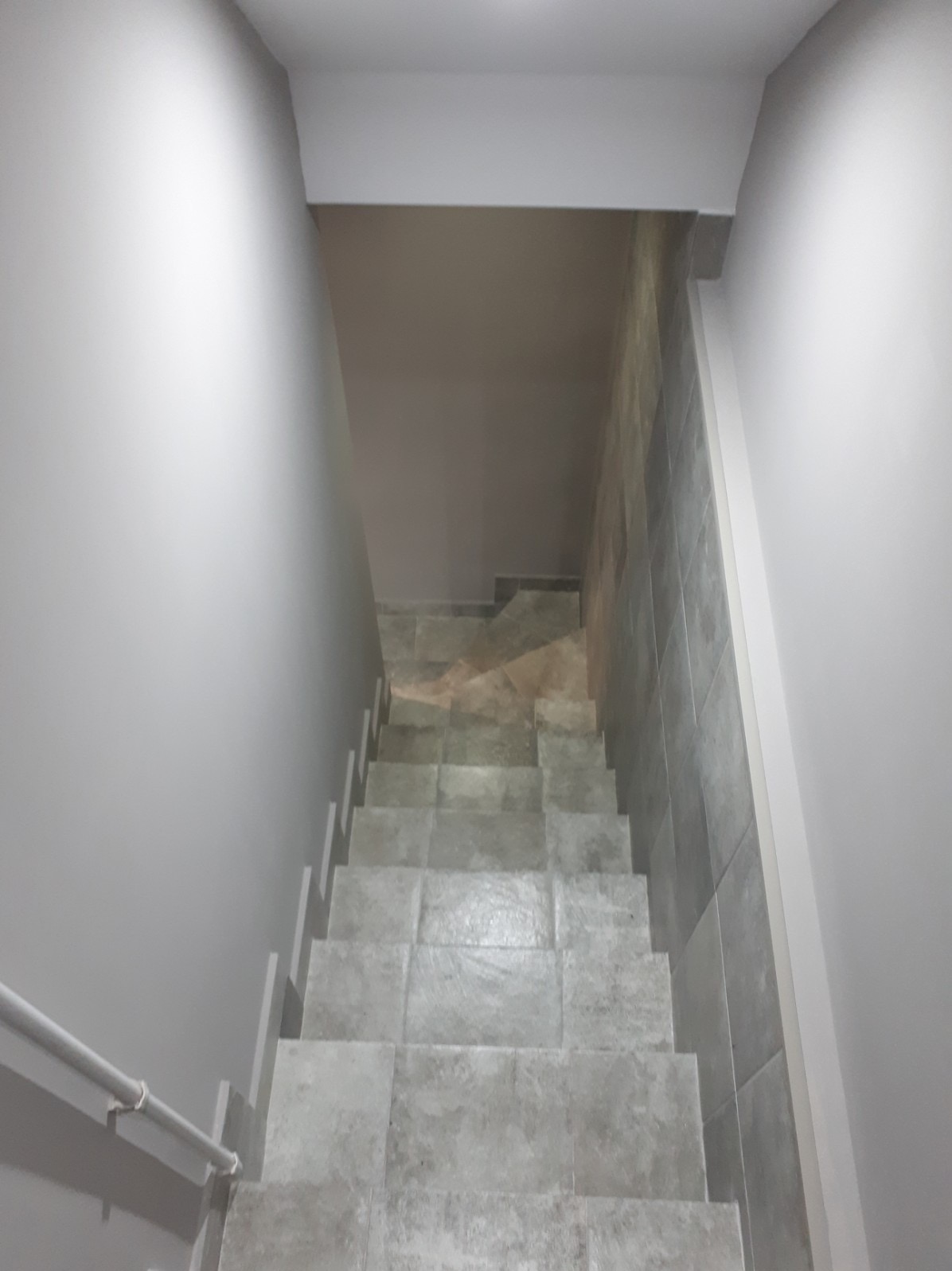 Schody wyłożone szarymi płytkami, widok z góry, ściany pomalowane na szaro, minimalistyczny design.