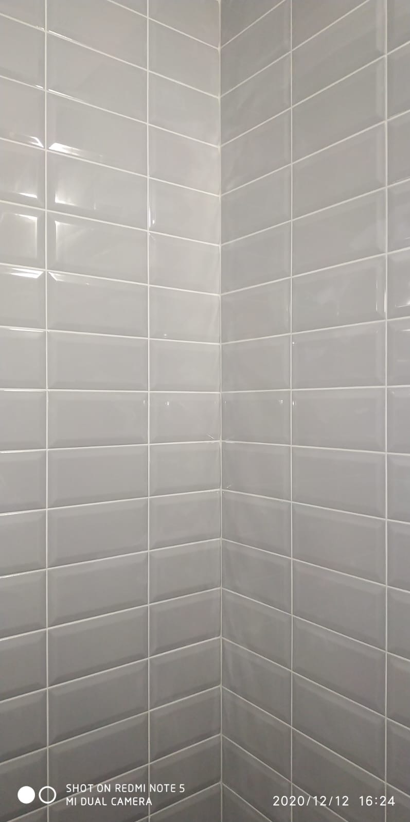 Świeżo położone szare, prostokątne płytki ścienne w stylu metro z białą fugą, tworzące narożnik w łazience.