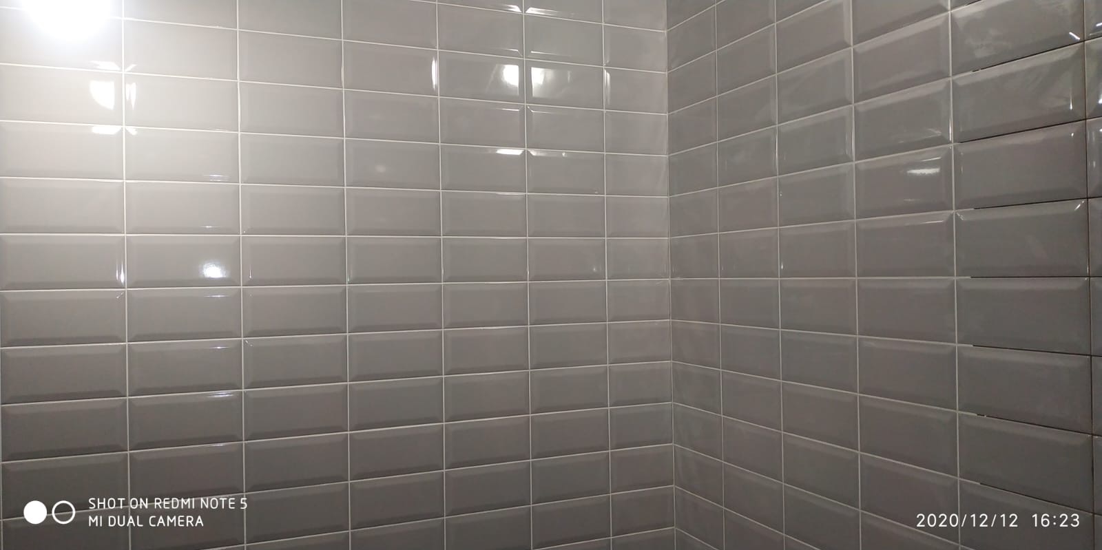 Ściana wyłożona szarymi, prostokątnymi płytkami ceramicznymi typu metro z jasną fugą, widoczny narożnik w pomieszczeniu.