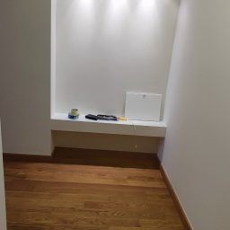 SaVo - Wnęka w świeżo pomalowanej ścianie z półką, na której leżą narzędzia, taśma malarska i skrzynka rewizyjna. Parkiet na podłodze.