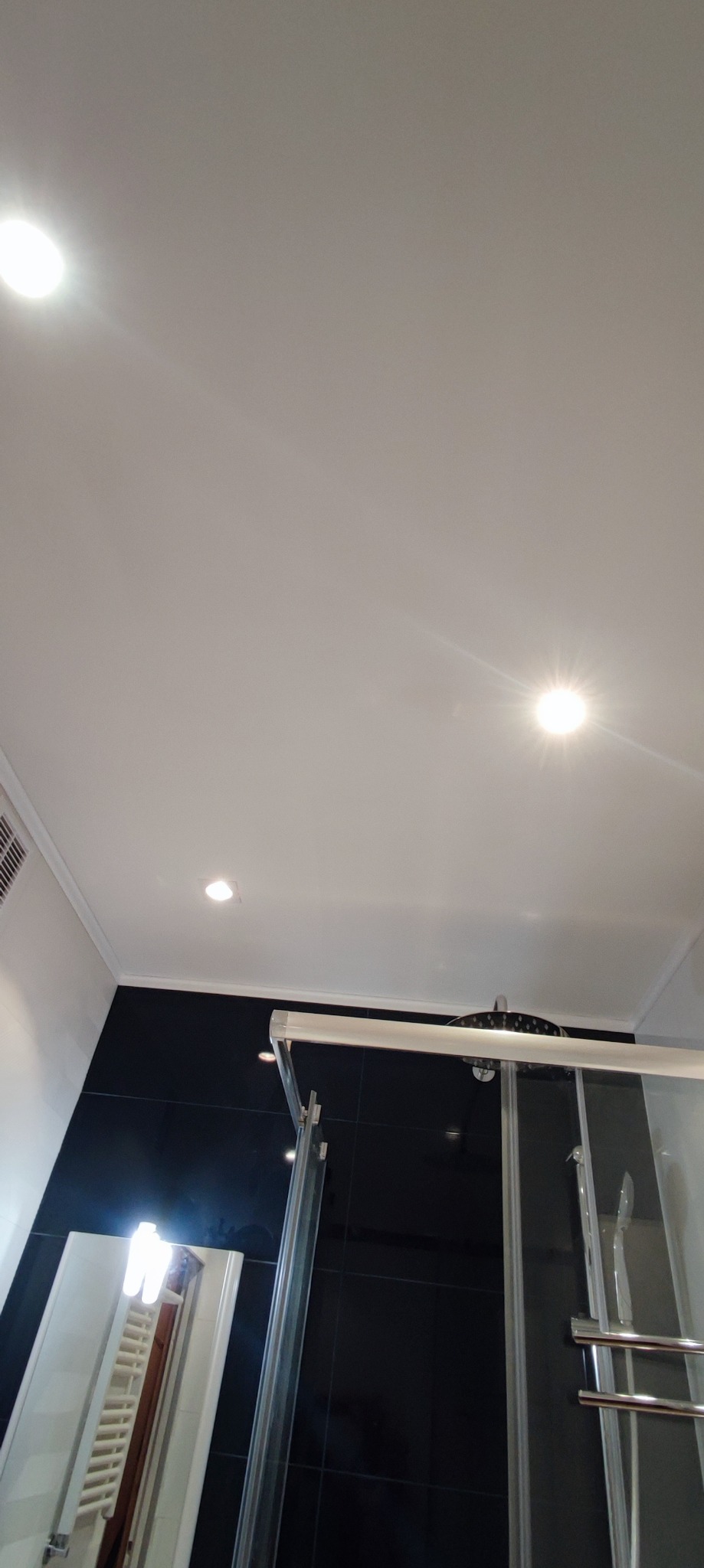 Nowoczesna łazienka z czarnymi płytkami, kabiną prysznicową ze szklanymi drzwiami i punktowym oświetleniem sufitowym.