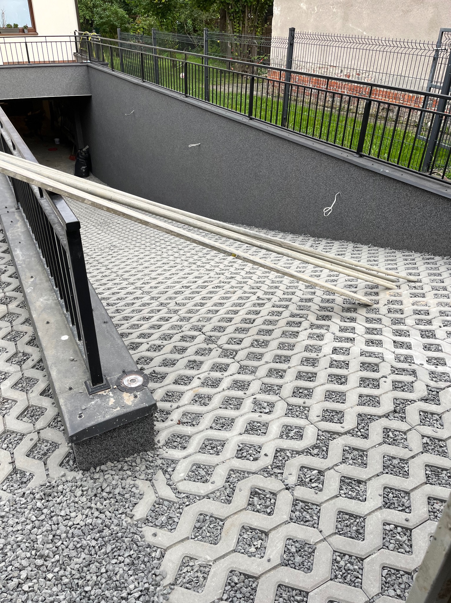 Ułożona szara kostka ażurowa z wypełnieniem żwirowym na podjeździe do garażu podziemnego, widoczne elementy ogrodzenia i przygotowane rury.