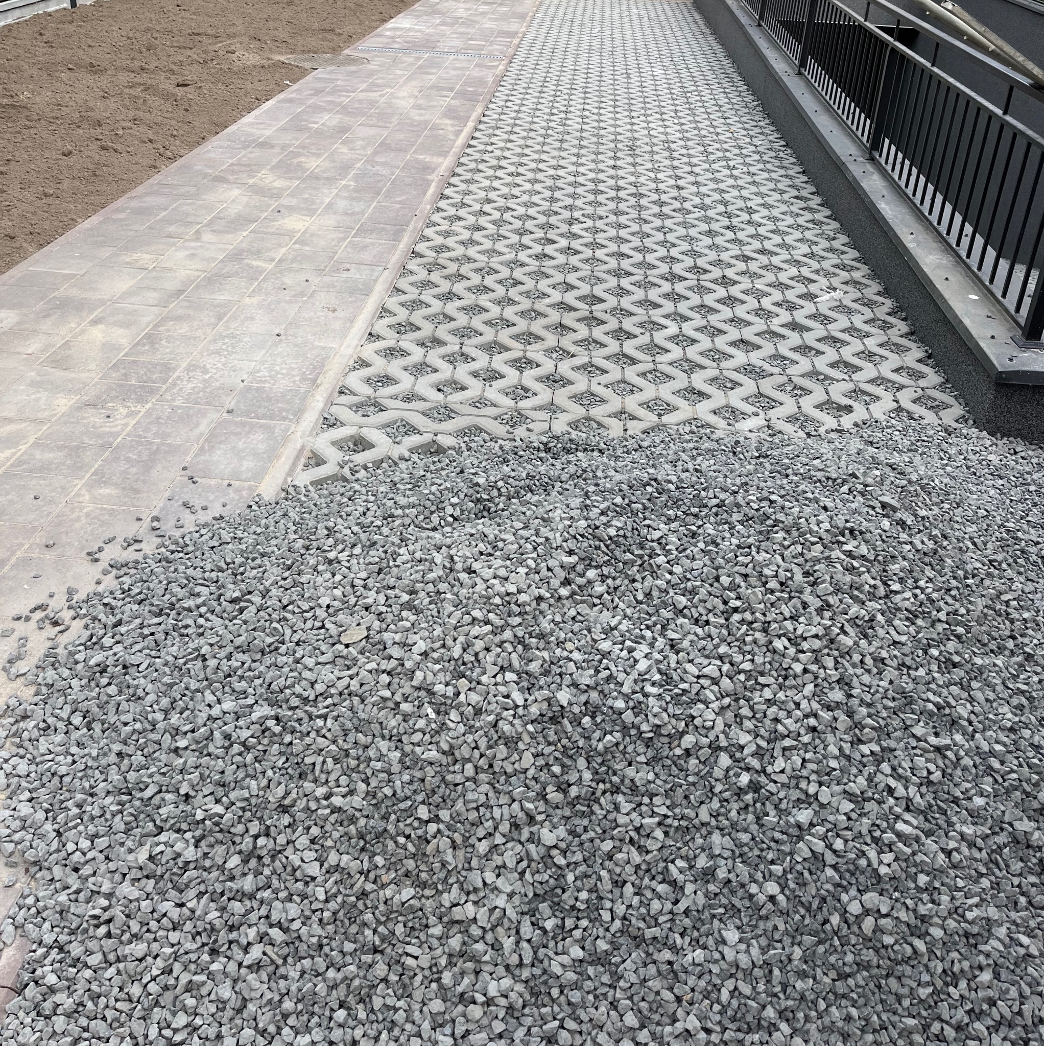 Układanie nawierzchni z kostki ażurowej wypełnionej grysem, widoczny stos grysu oraz obrzeże z kostki brukowej.