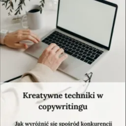 Osoba pracuje na laptopie, obok książka o kreatywnych technikach w pisaniu tekstów, filiżanka kawy, okulary i dekoracyjna gałązka na białym stole.