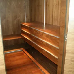 Wnętrze garderoby z drewnianymi elementami: szuflady z metalowymi akcentami, półki i podłoga z drewna o ciepłym odcieniu, widoczne elementy oświetlenia.