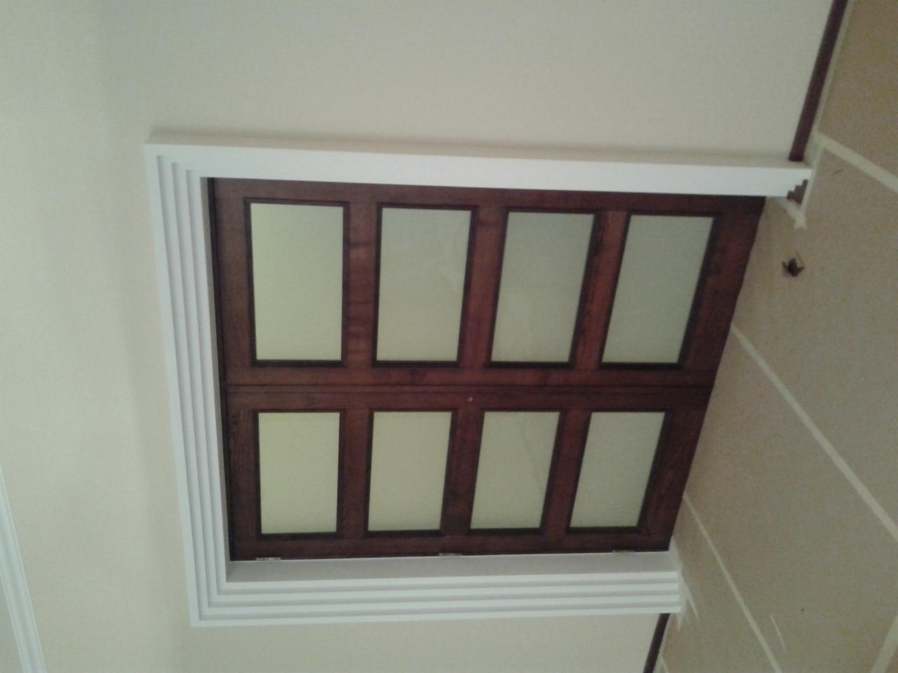 Kaseton sufitowy z drewnianą ramą i jasnymi panelami, otoczony białym, profilowanym obramowaniem. Widok z dołu, ukazujący detale wykończenia.