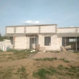 Surowy stan budowy domu z betonu komórkowego, widoczne szalunki nad otworami okiennymi i drzwiowymi, oraz sterta gruzu i materiałów budowlanych na pierwszym planie.