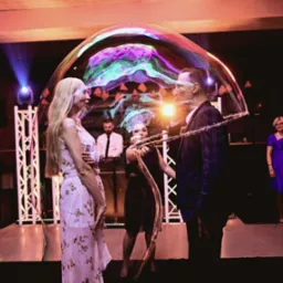 Para wewnątrz gigantycznej bańki mydlanej podczas występu, oświetlenie sceniczne w tle, kobieta tworzy bańki za pomocą specjalnego rekwizytu.