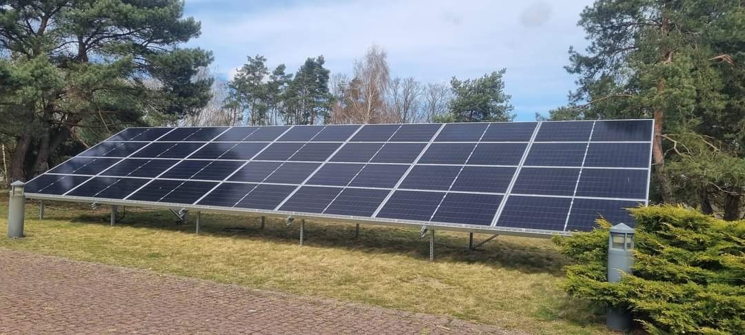 Instalacja fotowoltaiczna naziemna, panele ustawione na metalowej konstrukcji na trawniku, w tle drzewa.