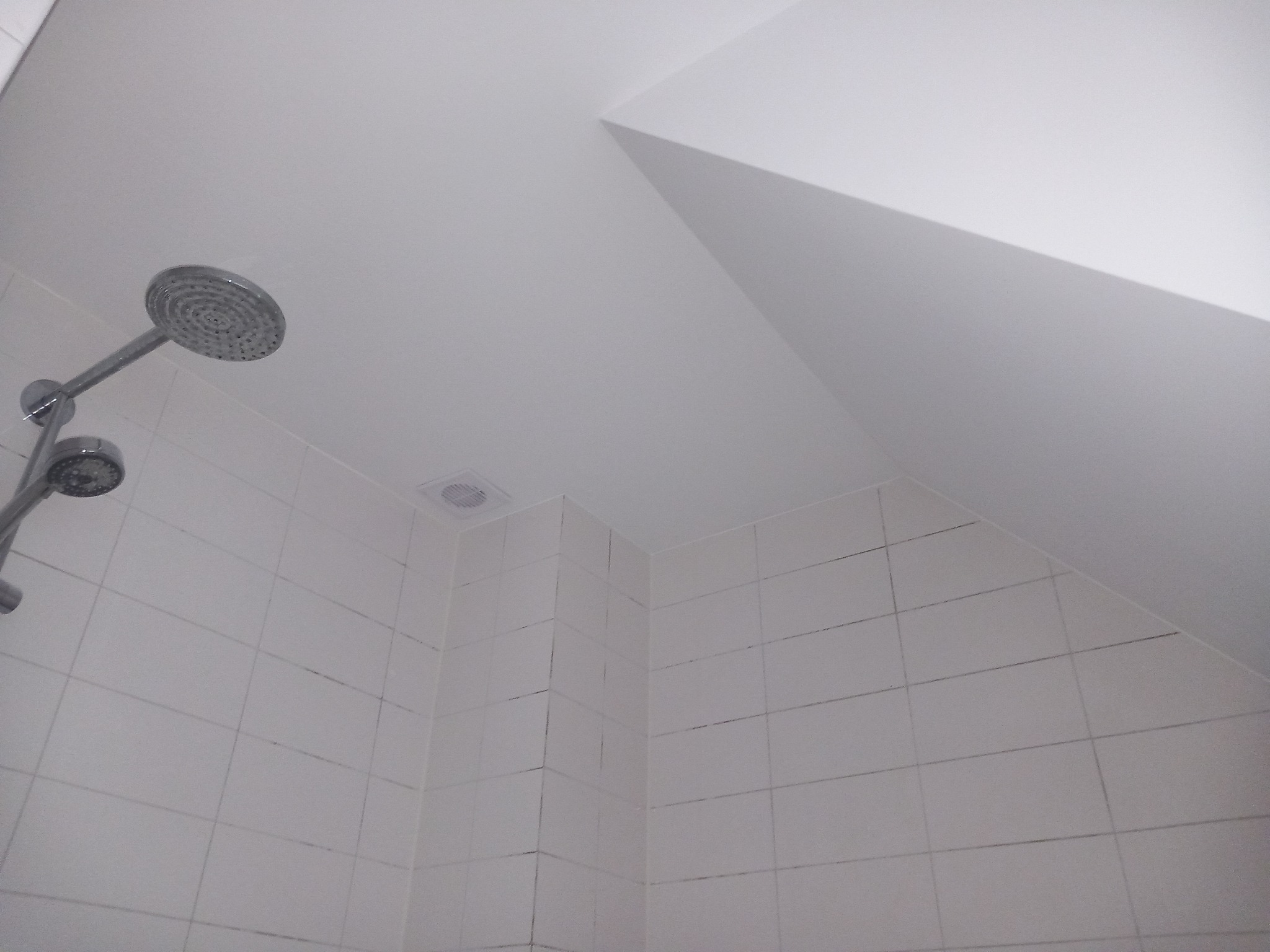 Biała kabina prysznicowa z widocznym panelem prysznicowym, białymi płytkami i skośnym sufitem.