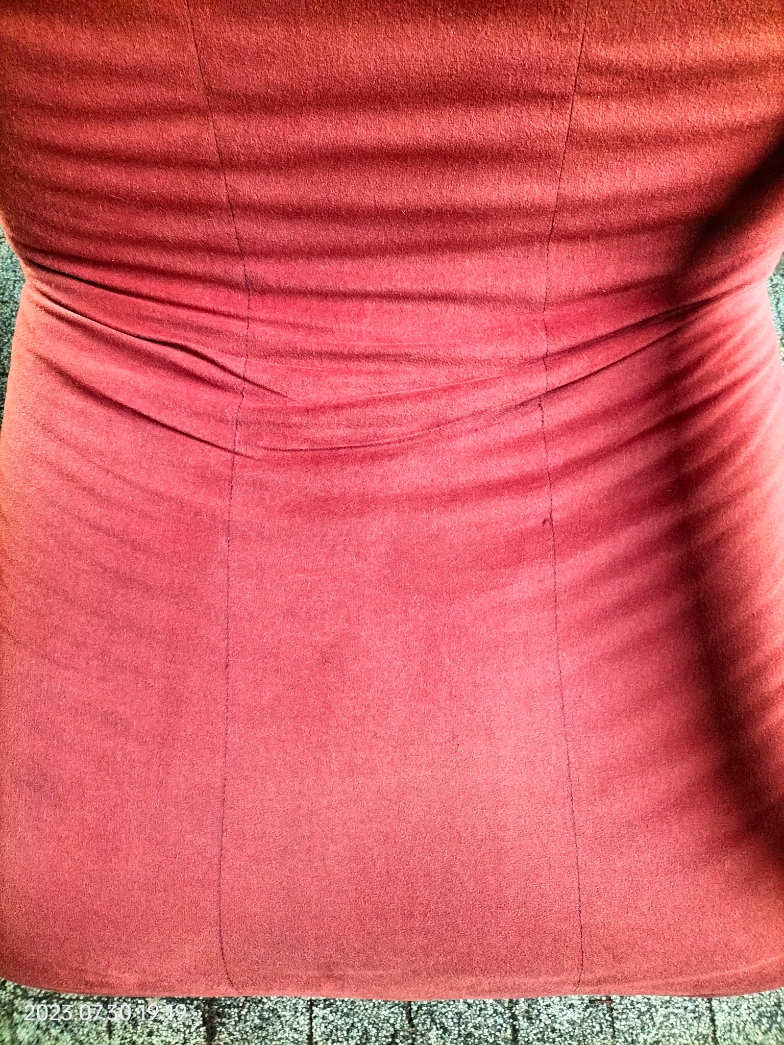 Czerwona, pluszowa tkanina z delikatnymi fałdami i centralnym szwem, leżąca na szarej, wzorzystej powierzchni.