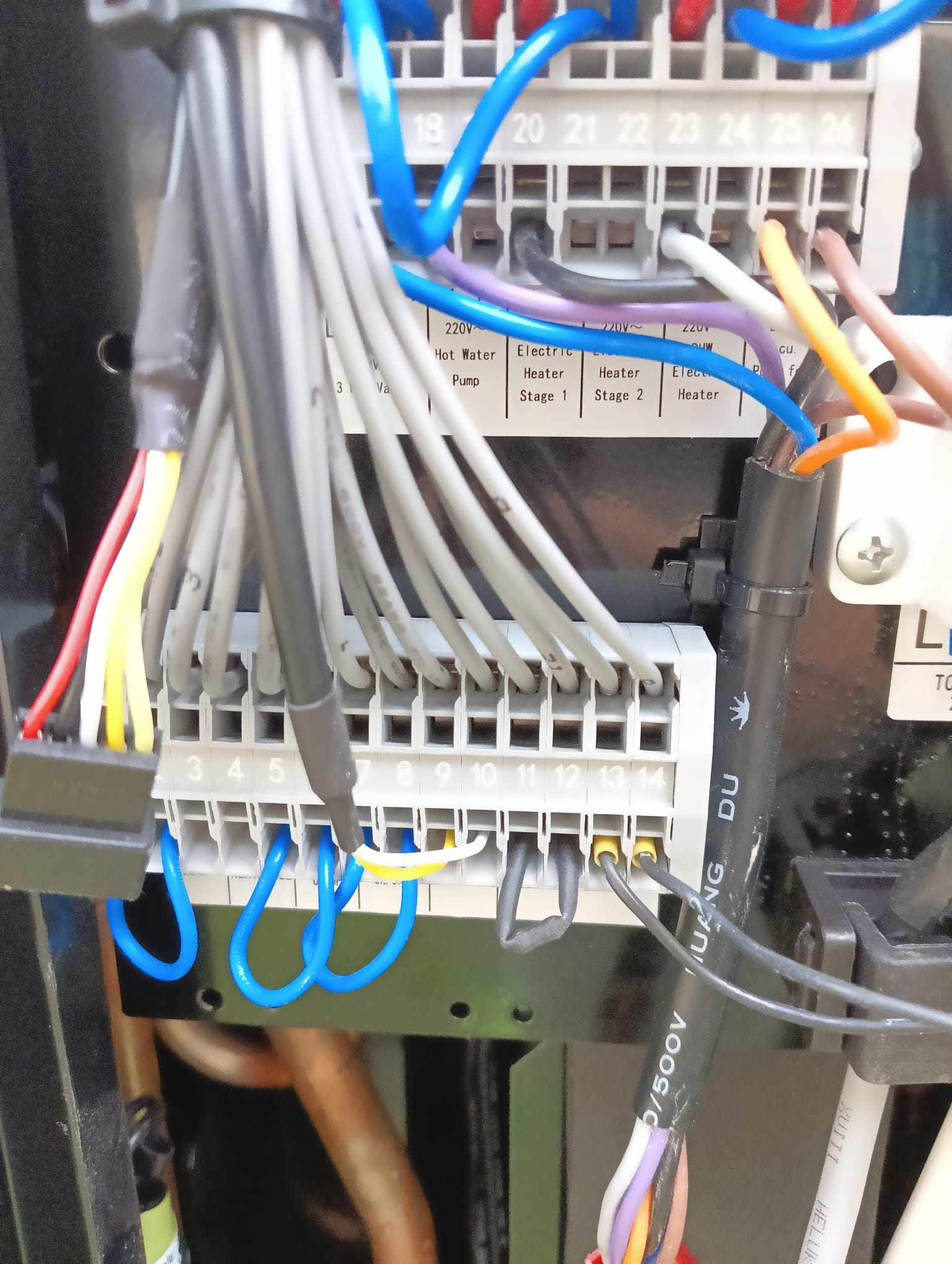 Szczegółowe ujęcie panelu sterowania z podłączonymi przewodami o różnych kolorach, widoczne zaciski i oznaczenia, instalacja elektryczna w trakcie podłączania.