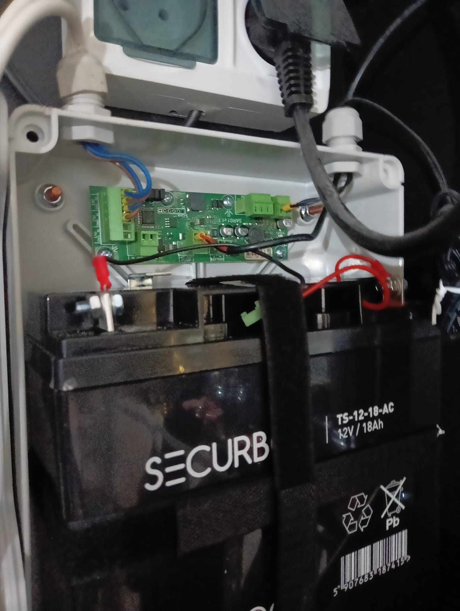 Podłączenie akumulatorów 12V do płytki sterującej wewnątrz skrzynki elektrycznej, widoczne kable zasilające i oznaczenia na akumulatorach SECURB.