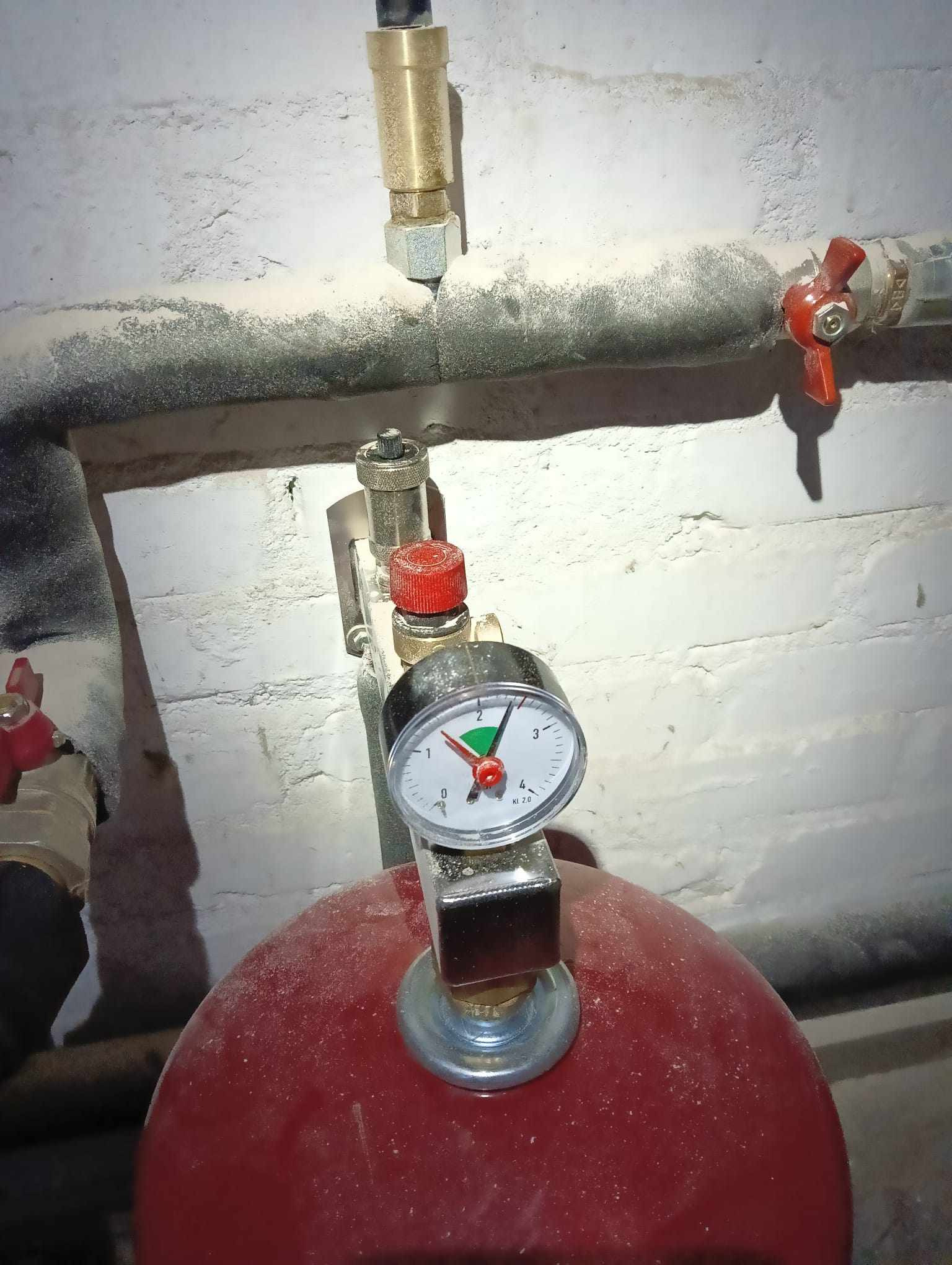 Czerwony zbiornik ciśnieniowy z manometrem wskazującym nieco ponad 2 bary, widoczne rury i zawory, wszystko pokryte warstwą kurzu.