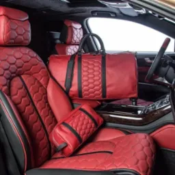 Czerwona skórzana tapicerka samochodowa z geometrycznym wzorem plastra miodu na siedzeniach, zagłówkach i torbach podróżnych wewnątrz luksusowego pojazdu.