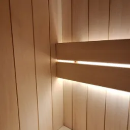 Wnętrze sauny wykończone jasnym drewnem, z podświetleniem LED za oparciem, ukazujące minimalistyczny design i czystość.