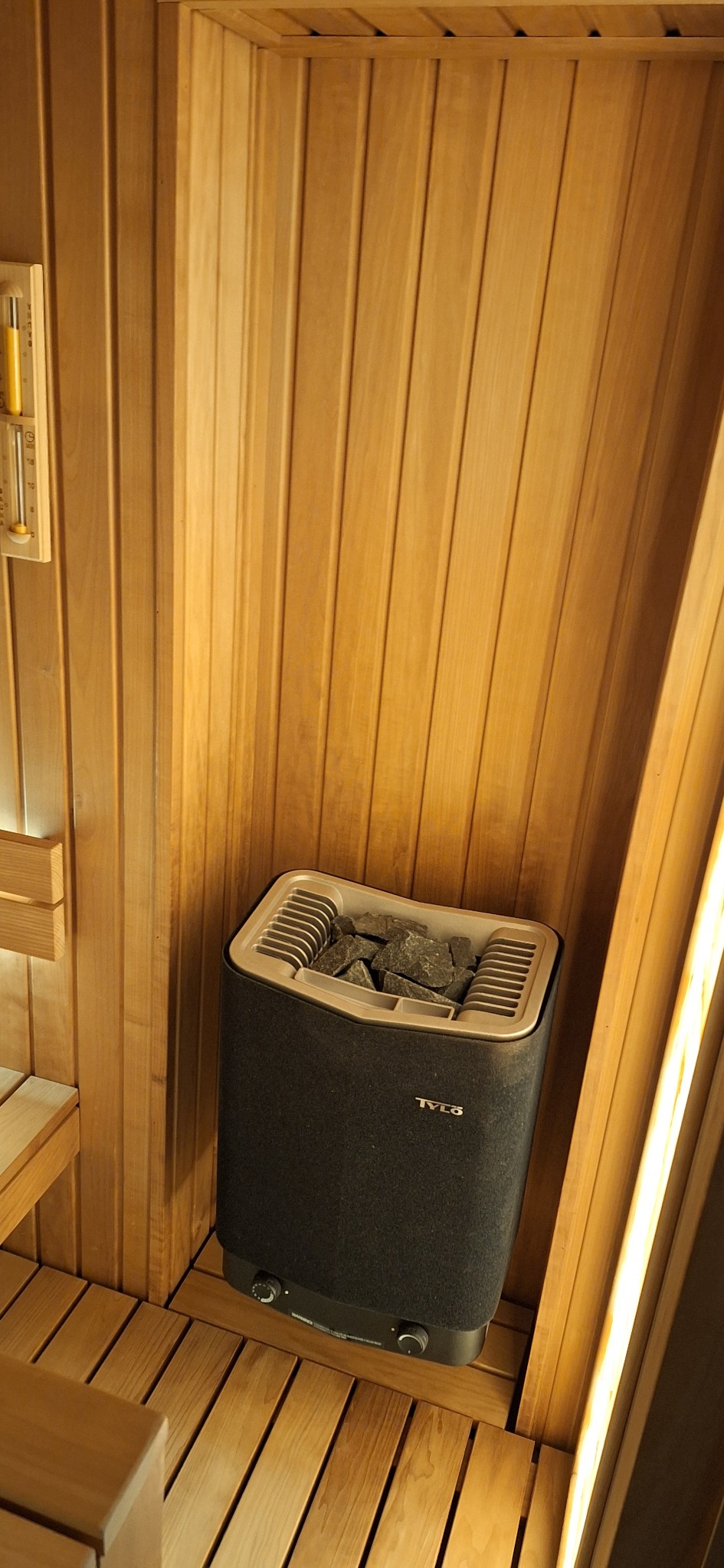 Wnętrze drewnianej sauny z piecem marki Tylo wypełnionym kamieniami w rogu pomieszczenia.