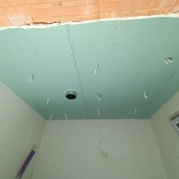 Bud Wr - Niebieska płyta kartonowo-gipsowa na suficie z widocznymi przewodami elektrycznymi i otworem pod oświetlenie, w surowym stanie wykończenia wnętrza.