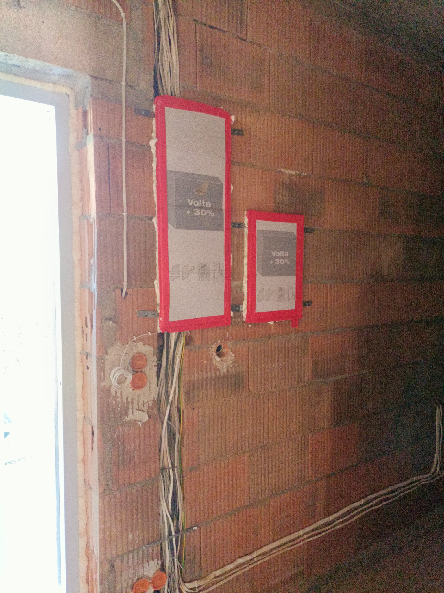 Instalacja elektryczna w trakcie montażu: przewody, puszki i reklama Volta +30% na ścianie z cegły dziurawki.