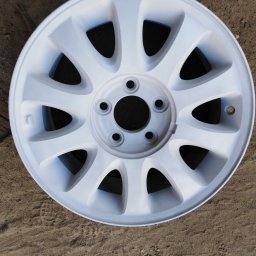 Bartłomiej Lorenc - Biała felga samochodowa po malowaniu proszkowym, leżąca na ziemi z odciskiem bieżnika opon.