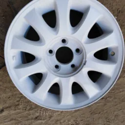 Biała felga samochodowa po malowaniu proszkowym, leżąca na ziemi z odciskiem bieżnika opon.