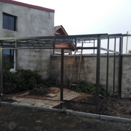 Bartłomiej Lorenc - Metalowa konstrukcja w trakcie budowy na posesji, widoczne elementy szkieletu, betonowe płyty i drabina oparta o ścianę.