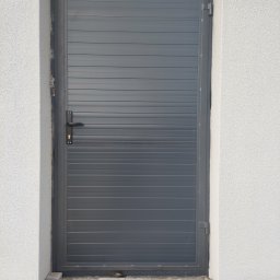 Bartłomiej Lorenc - Szara brama wjazdowa z poziomymi panelami, zamontowana w białym murze z kostką brukową u podstawy.