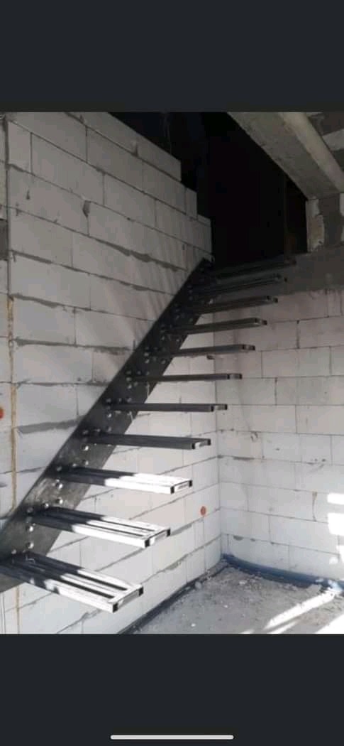 Surowe, metalowe schody wewnętrzne bez poręczy, zamontowane w surowym stanie budynku z białych bloczków.