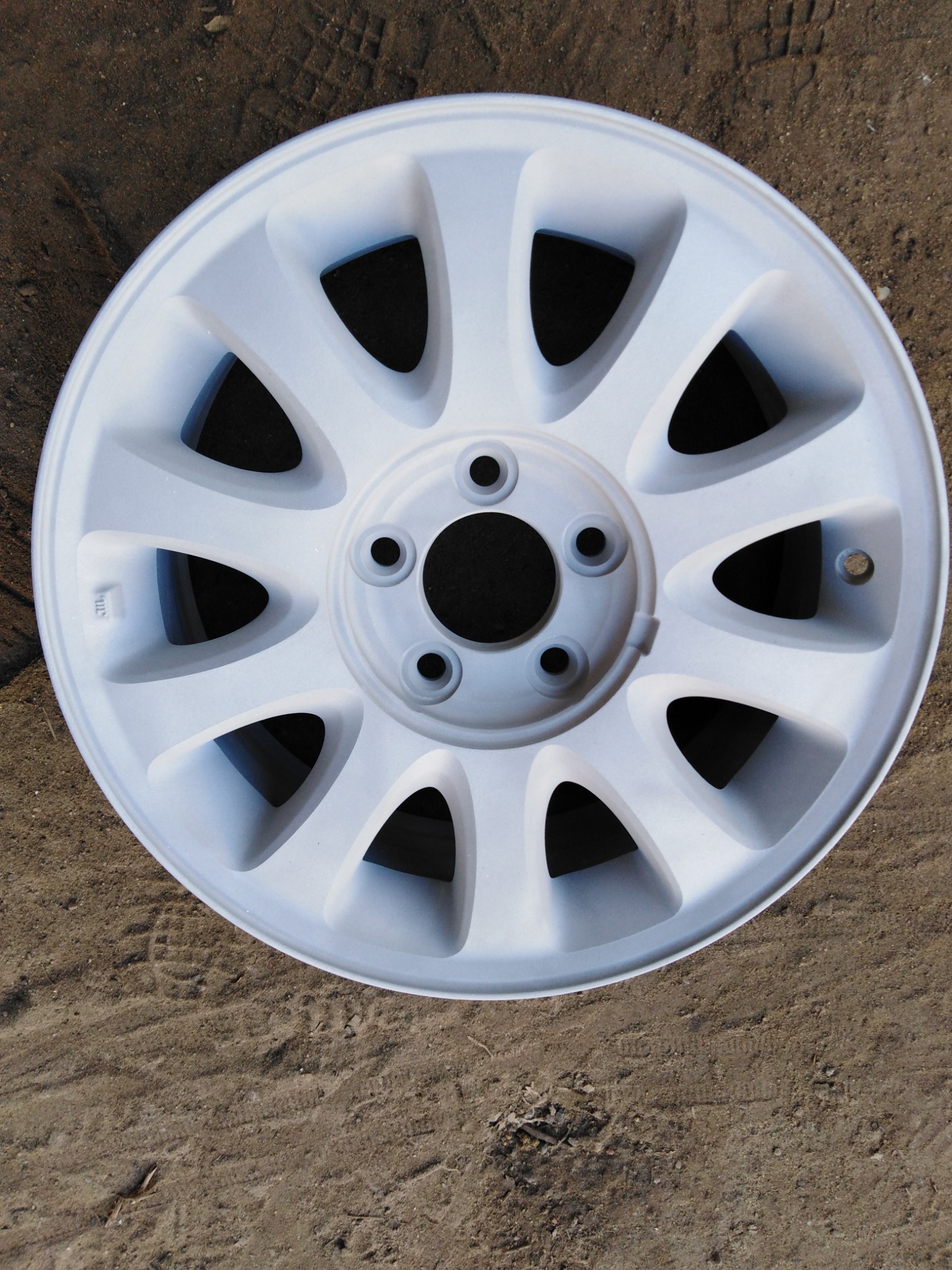 Biała felga samochodowa po malowaniu proszkowym, leżąca na ziemi z odciskiem bieżnika opon.