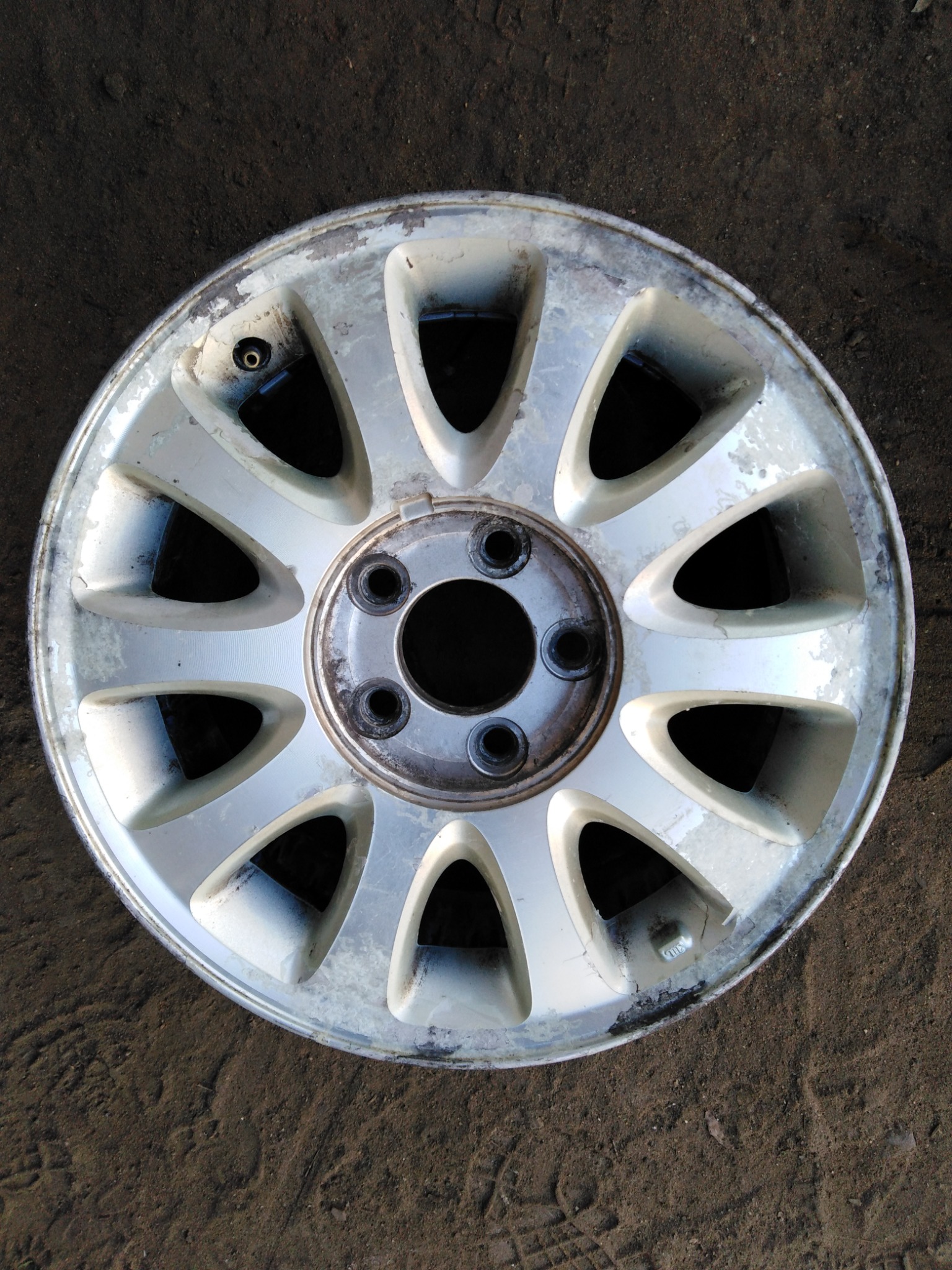 Używana, aluminiowa felga samochodowa z widocznymi śladami korozji i zarysowaniami, leżąca na ziemi.